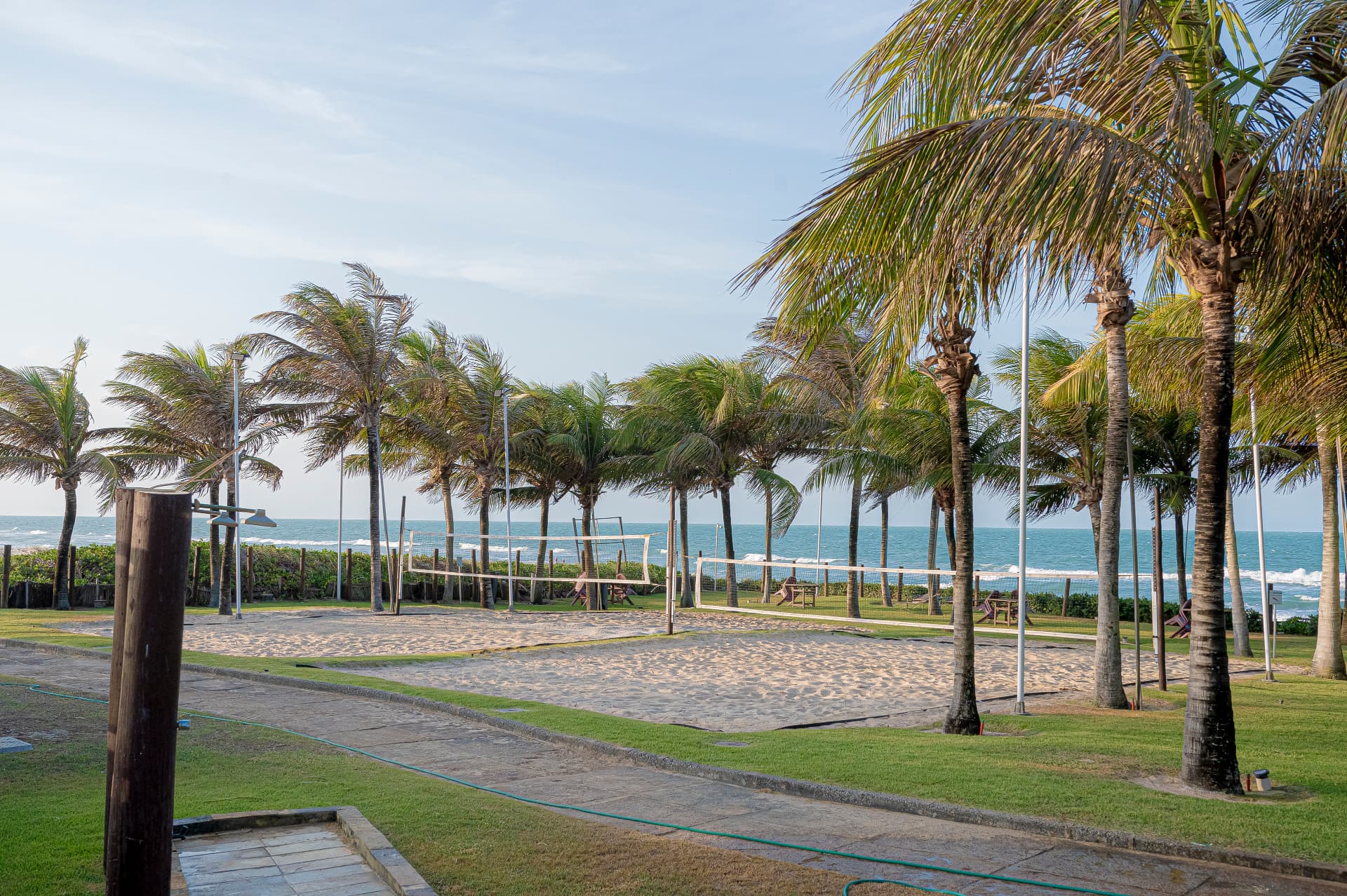 Quadras de vôlei de praia com coqueiros e mar ao fundo